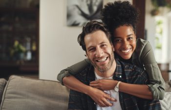 Smile, hug and couple with portrait on sofa for marriage bonding, partnership and romance together. Happy, man and woman with affection on couch at home for love, trust and connection on weekend