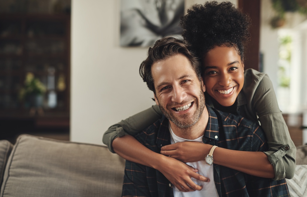 Smile, hug and couple with portrait on sofa for marriage bonding, partnership and romance together. Happy, man and woman with affection on couch at home for love, trust and connection on weekend